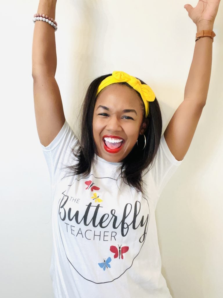 Tanya G. Marshall, founder of The Butterfly Teacher, smiling with arms raised in a Butterfly Teacher shirt